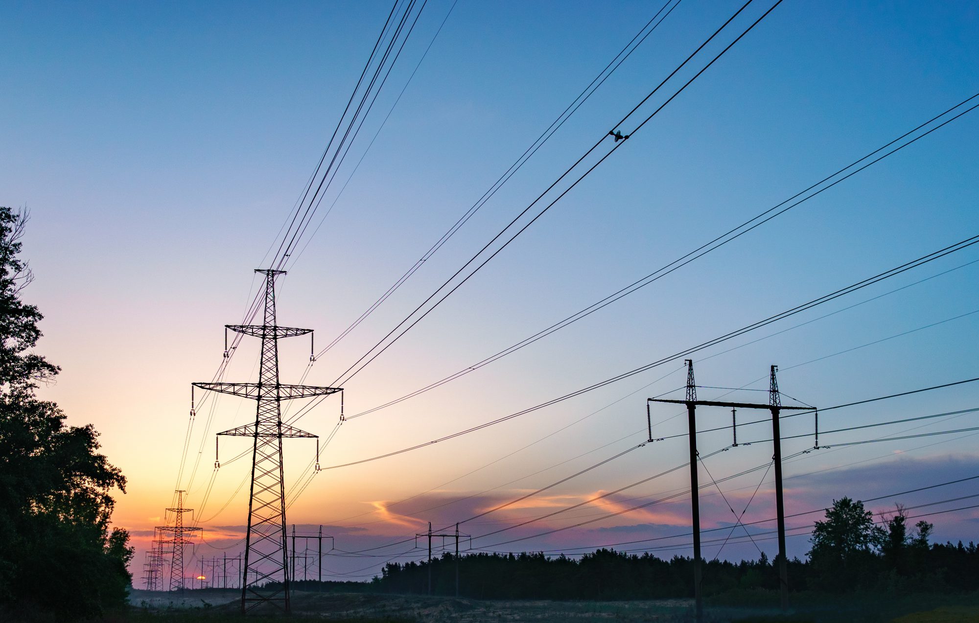 Sun setting behind the silhouette of electricity pylons