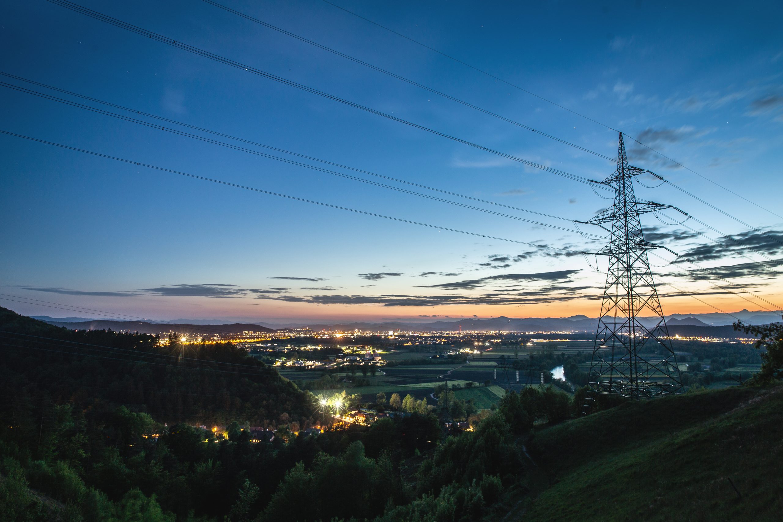 Smart grid in the sunset with a larger city in the background. The city is full of lights and the sky is darkblue with a bit of purple and orange.