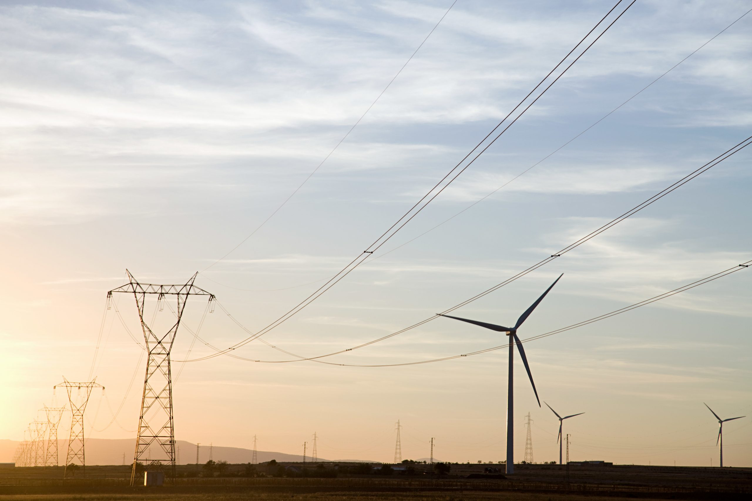 Electric grid with wind turbines in the background.