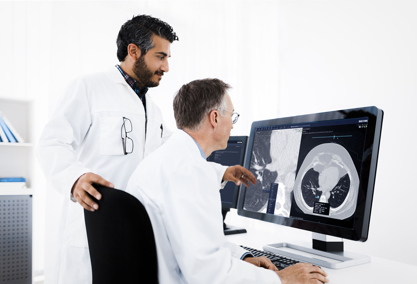 Two male radiologists discussing a radiology case in front of a monitor